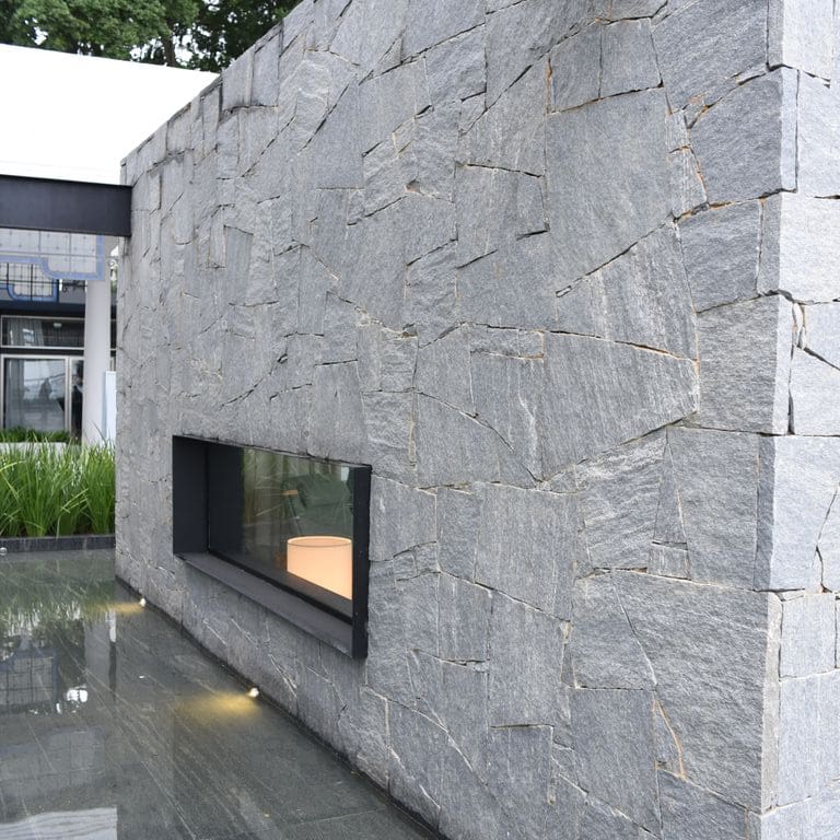 Application image for Brazilian Lucerna Gneiss. The image shows this material being used in a full bed veneer application. The surface finish shown is split-face. The dominant color shown is gray. The color mix creates a cool feeling.