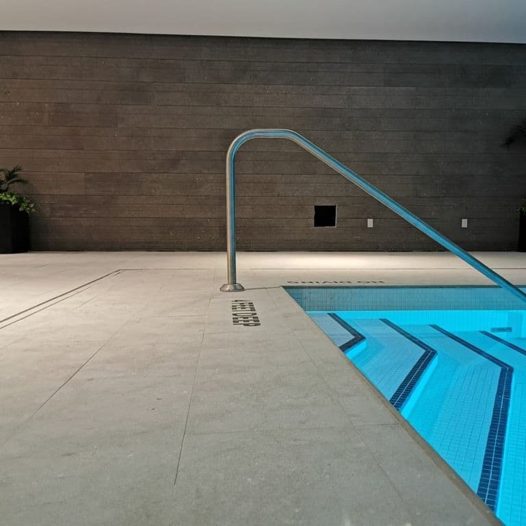 Application image for Grigio Olivo Limestone. The image shows this material being used for pool coping and pool deck pavers. The surface finish shown is flamed. The dominant color shown is gray; with beige, brown and tan secondaries. The color mix creates a warm feeling. Cloudy color pattern. Contains mineral inclusions.
