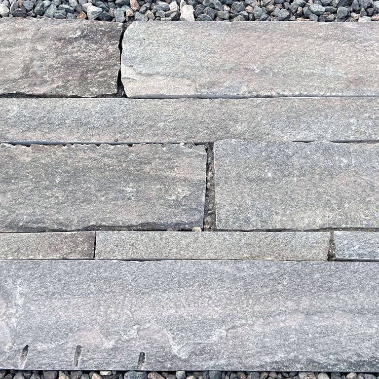 Feature image for Reclaimed Quartzite Plank Pavers - Blue/Gray. The image shows this material being used in a patio pavers application. The surface finish shown is a combination of split-face with flat plane, weathered and worn. Dominant colors shown are blue and gray; with beige, brown, green, orange/rust, pink, purple, white, tan and cream secondaries. Regular, linear, fine speckled and blotched color patterns. Contains some mica.
