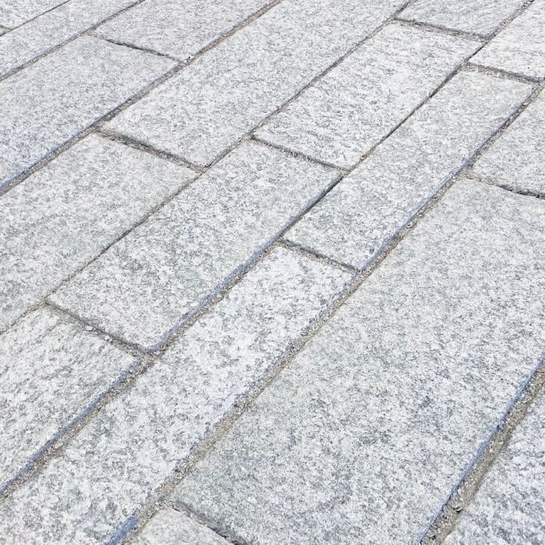 Best close-up image for Pietra Italia Gneiss - Blue. The image shows this material being used in a patio pavers application. The surface finish shown is flamed. Dominant colors shown are gray and white; with blue, pink and cream secondaries. The color mix creates a cool feeling. Fine speckled and random color patterns. Contains some mica and mineral inclusions.