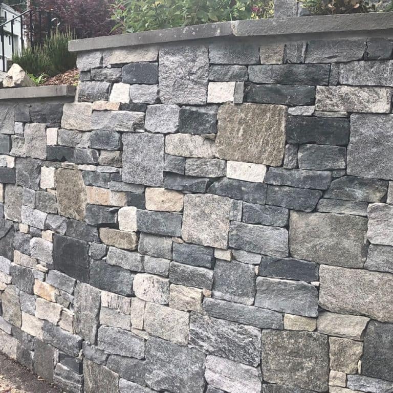 Application image for Windsor Granite Thin Veneer. The image shows this material being used for thin veneer and retaining wall. The surface finish shown is . The dominant color shown is gray. The color mix creates a warm feeling. Regular, streaked and random color patterns.