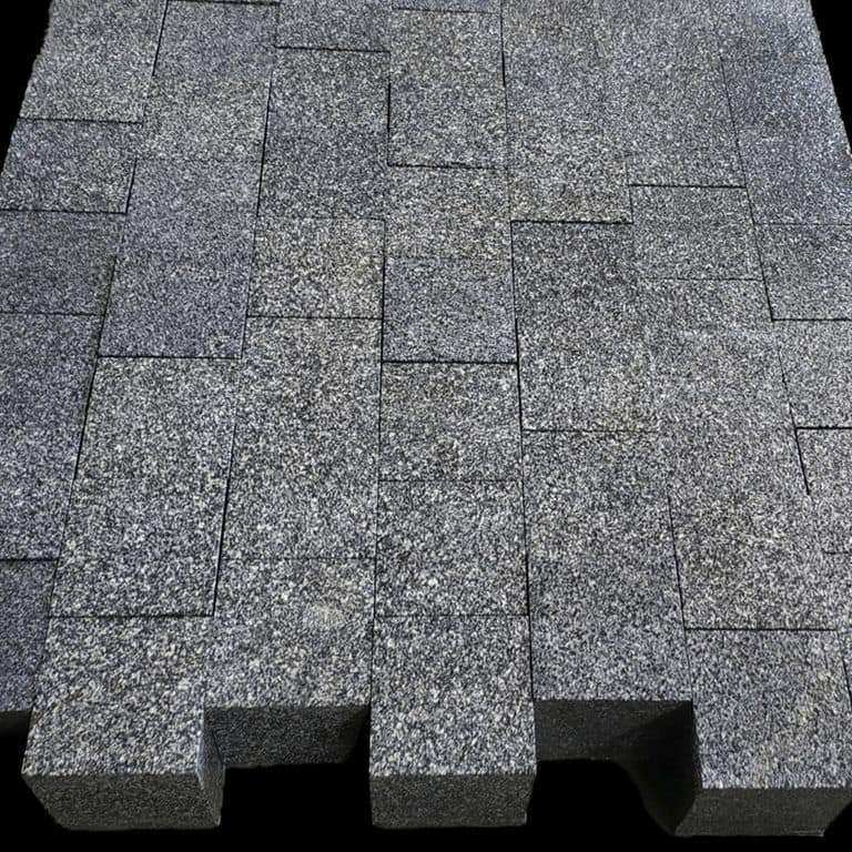 Feature image for Tai Black Granite. The surface finish shown is a combination of flamed and sawn. The dominant color shown is gray. The color mix creates a cool feeling. Regular and speckled color patterns.