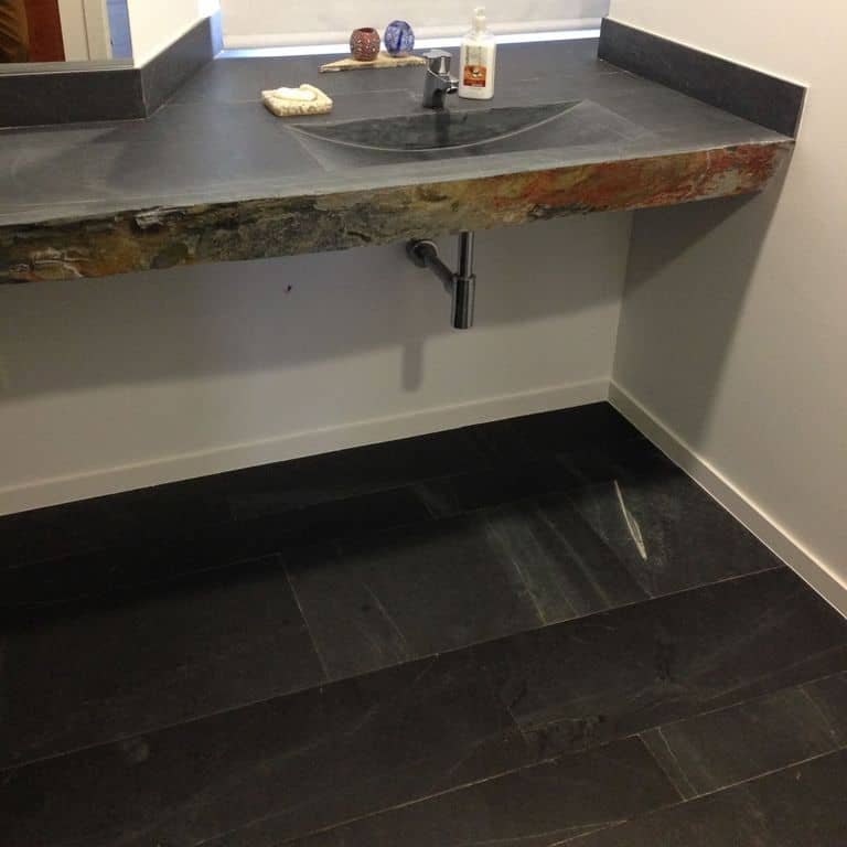 Application image for Iberian Gray Slate. The image shows this material being used for interior floor, countertop slabs and sinks. The surface finish shown is a combination of flamed, honed and natural. Dominant colors shown are black and gray. Linear and blotched color patterns.