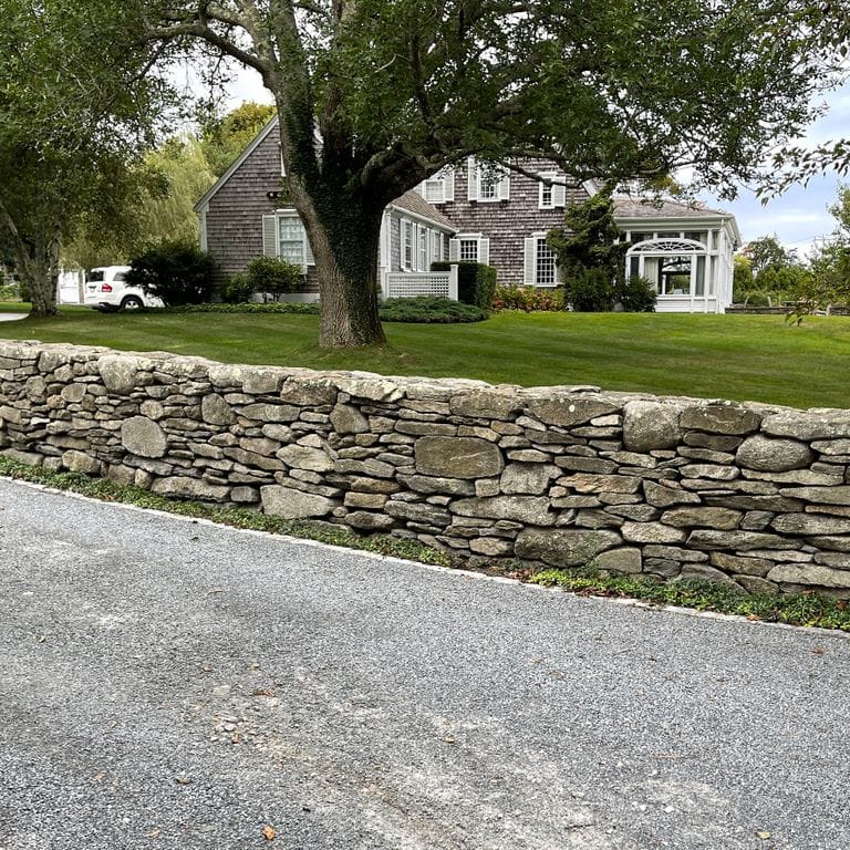 Feature image for Fieldstone - New England Flats. The image shows this material being used in a landscape wallstone application. The surface finish shown is weathered. Dominant colors shown are brown and tan; with green and gray secondaries. The color mix creates a warm feeling.