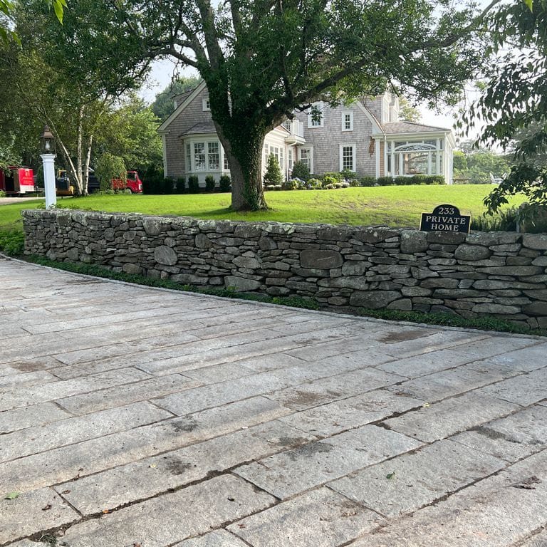 Application image for New England Fieldstone Flats. The image shows this material being used in a landscape wallstone application. The surface finish shown is weathered. The dominant color shown is gray.