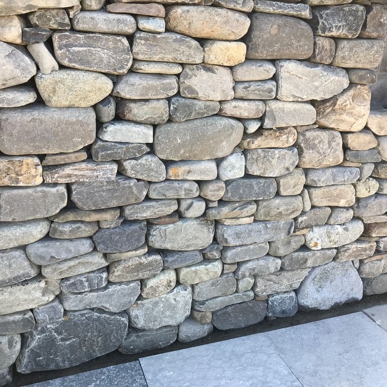 Application image for New England Fieldstone Flats. The image shows this material being used in a thin veneer application. The surface finish shown is weathered. The dominant color shown is gray.