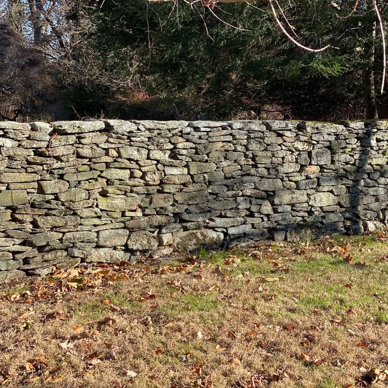 Application image for Fieldstone - New England Flats. The image shows this material being used in a landscape wallstone application. The surface finish shown is weathered. Dominant colors shown are brown, gray and tan. The color mix creates a warm feeling.