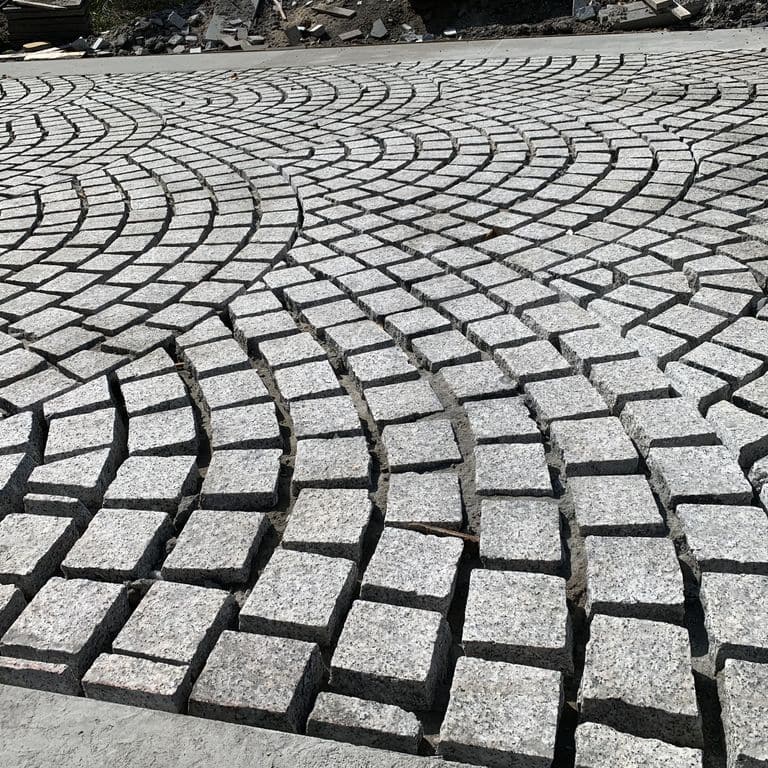 Feature image for Superior Snow Granite. The image shows this material being used in a driveway pavers application. Dominant colors shown are gray and white. The color mix creates a cool feeling.
