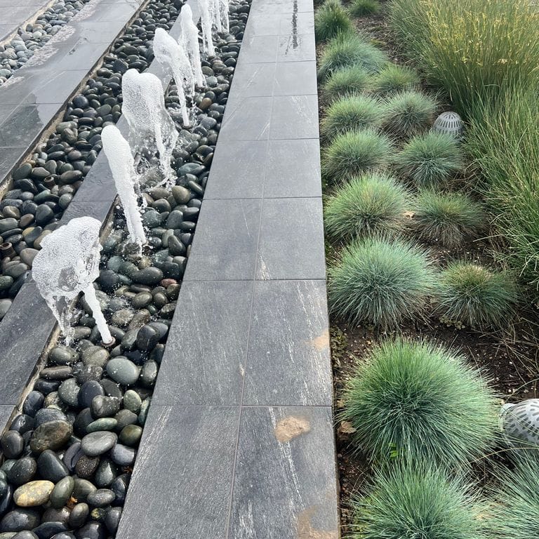 Application image for Strata Mist Cross-Cut Gneiss. The image shows this material being used for water features and public area. The dominant color shown is gray. The color mix creates a cool feeling.