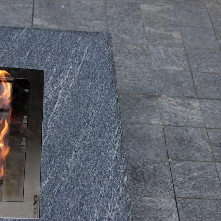 Application image for Strata Mist Cross-Cut Gneiss. The image shows this material being used for outdoor fire concepts and patio pavers. The dominant color shown is gray. The color mix creates a cool feeling.