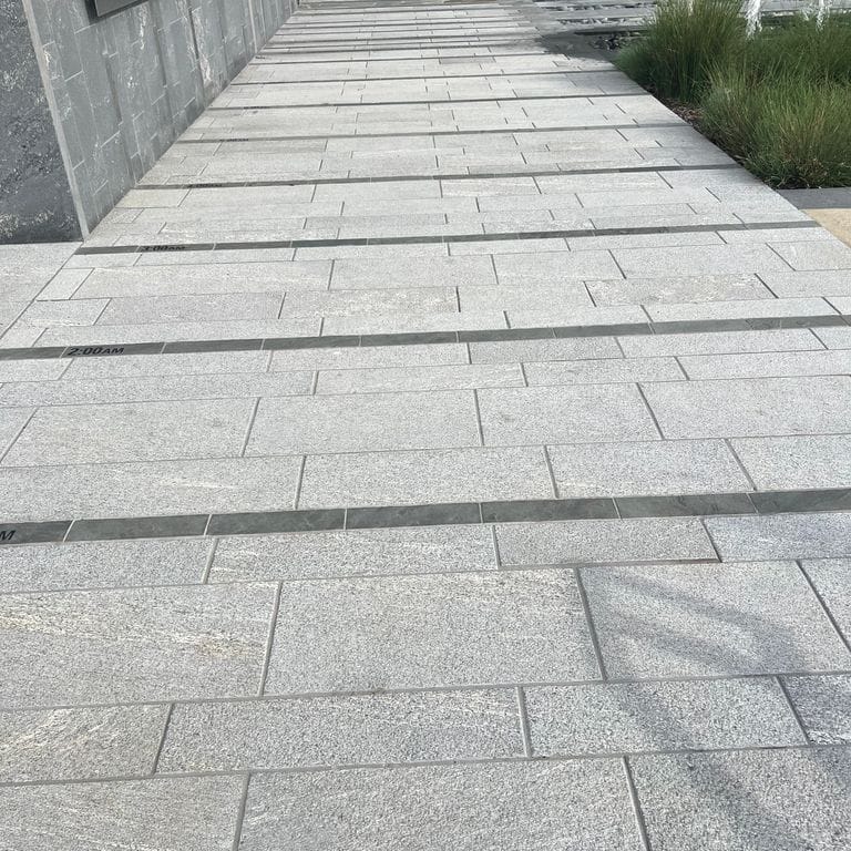 Application image for Strata Mist Cross-Cut Gneiss. The image shows this material being used for patio pavers and public area. The dominant color shown is gray. The color mix creates a cool feeling.