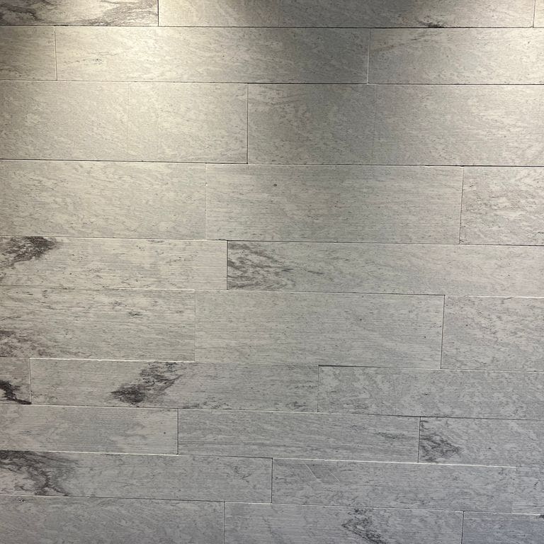 Application image for Strata Snow Gneiss. The image shows this material being used in an interior cladding application. The surface finish shown is honed. Dominant colors shown are gray and white. The color mix creates a warm feeling.