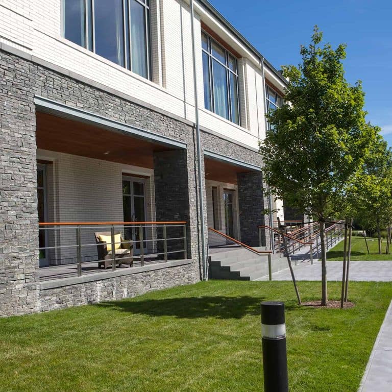 Application image for Greenwich Gray Granite. The image shows this material being used for full bed veneer and thin veneer. The surface finish shown is split-face. Dominant colors shown are black and gray.