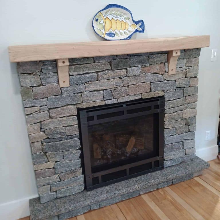 Application image for Vineyard Granite. The image shows this material being used in a fireplace surround application. The surface finish shown is split-face. The dominant color shown is gray. The color mix creates a cool feeling.
