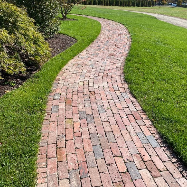 Feature image for Reclaimed Brick. The image shows this material being used in a path pavers application. Dominant colors shown are pink and red; with brown, gray, orange/rust, purple and tan secondaries. The color mix creates a warm feeling. Regular color pattern.