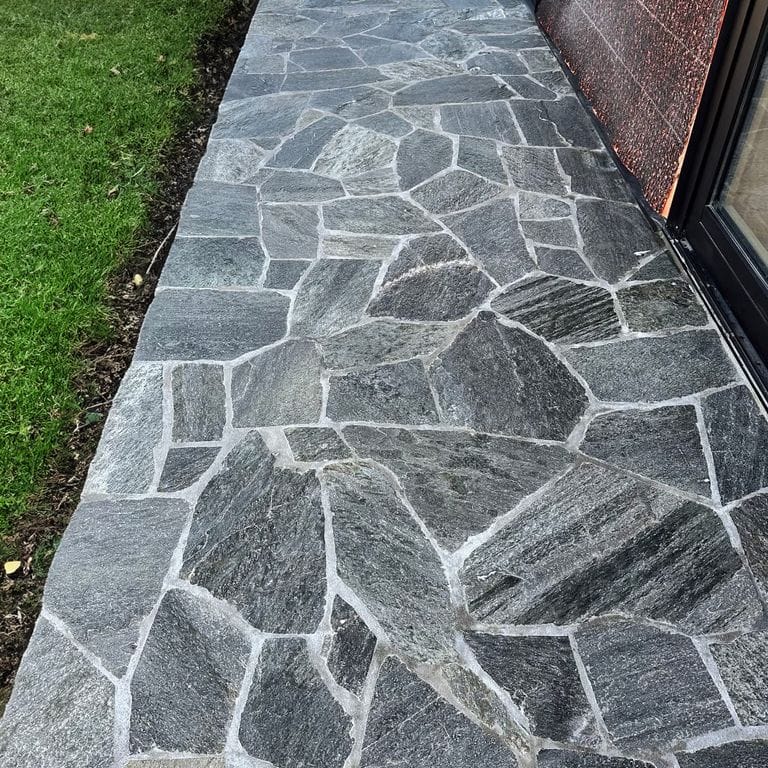 Feature image for Oakley Stone - Charcoal. The image shows this material being used in a patio pavers application. The surface finish shown is natural cleft. The dominant color shown is gray. The color mix creates a cool feeling.