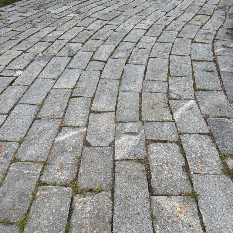 Application image for Reclaimed Granite Junior Curbstone. The image shows this material being used in a driveway pavers application. The surface finish shown is . The dominant color shown is gray. The color mix creates a warm feeling.