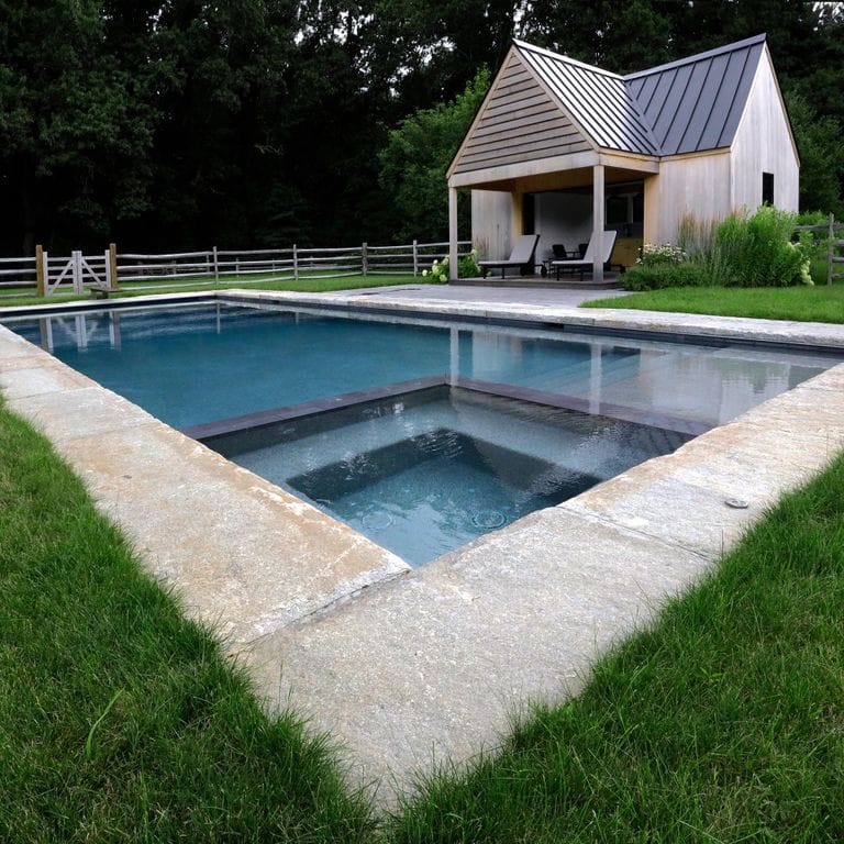 Application image for Reclaimed Granite Curbstone - Jumbo. The image shows this material being used in a pool coping application. The surface finish shown is a combination of split-face with flat plane, weathered and worn. Dominant colors shown are beige and gray; with orange/rust, purple, white, tan and cream secondaries. The color mix creates a warm feeling. Regular and fine speckled color patterns.