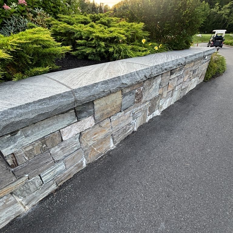 Application image for Mystic Mountain Granite - Flamed. The image shows this material being used in a wallstone cap application. The surface finish shown is flamed. The dominant color shown is gray. The color mix creates a warm feeling.