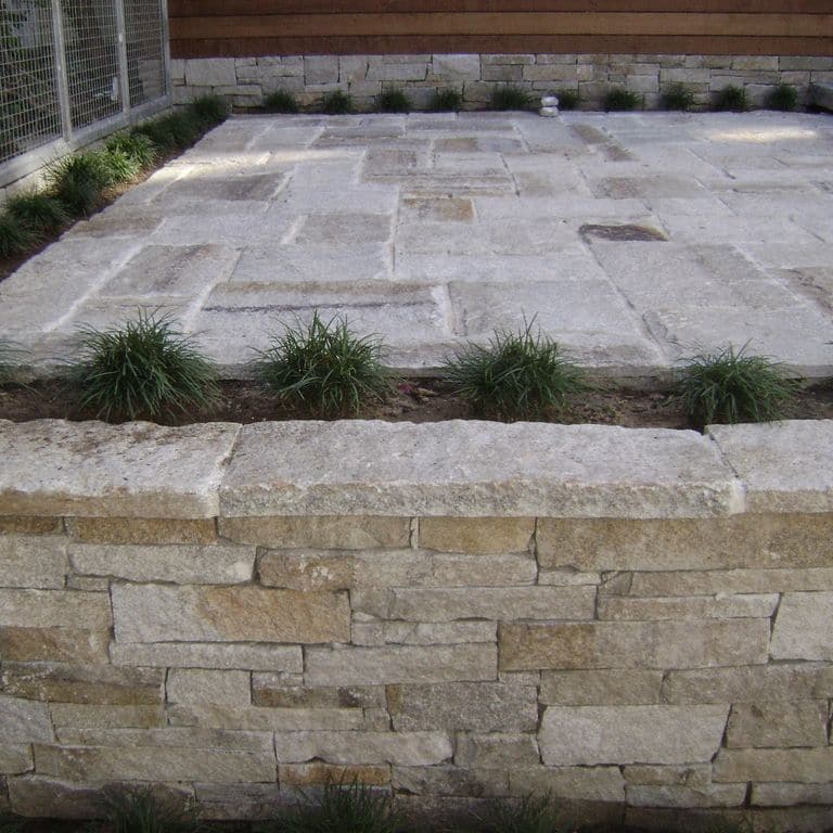 The image shows this material being used in a wallstone cap application. The dominant color shown is gray; with brown, orange/rust, white and tan secondaries. Regular and fine speckled color patterns.