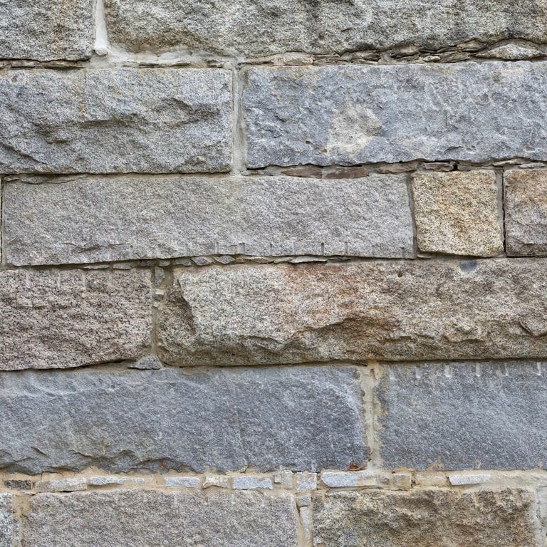 Best close-up image for Granite- Reclaimed Bridge Blocks. The surface finish shown is . The dominant color shown is gray; with beige, blue, brown, green, orange/rust, purple, white and tan secondaries. Exhibits "movement". Fine speckled, speckled, blotched and cloudy color patterns.