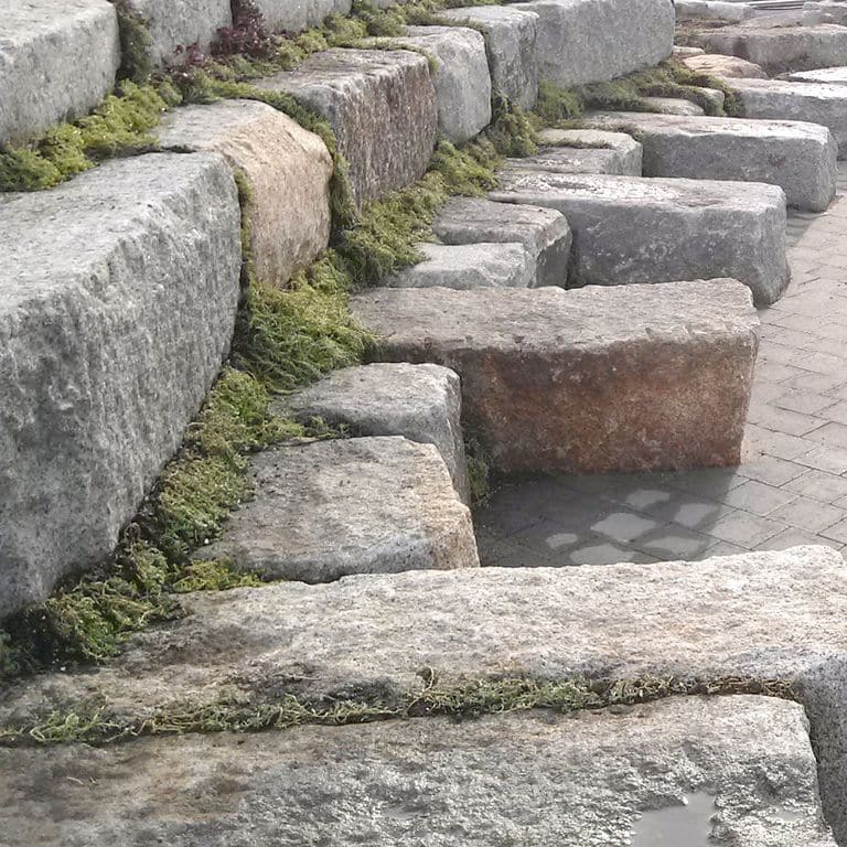 Application image for Reclaimed Granite Bridge Blocks. The image shows this material being used for seating &amp; benches and landscape wallstone. The surface finish shown is weathered. The dominant color shown is gray; with beige, brown, white and tan secondaries. Regular and blotched color patterns.