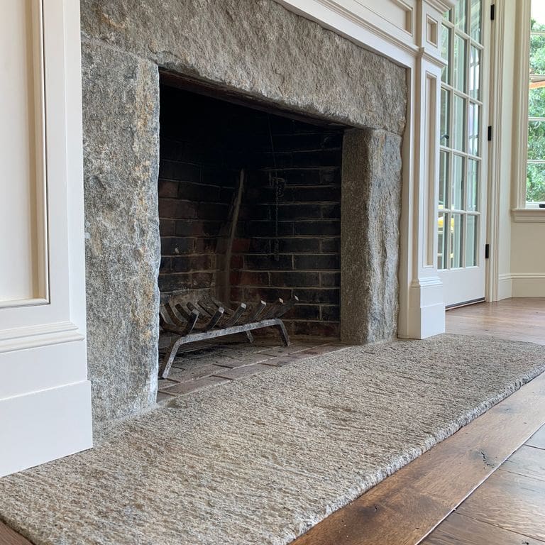 Application image for Reclaimed Granite Bridge Blocks. The image shows this material being used in a fireplace hearth application. The dominant color shown is gray; with beige and white secondaries. The color mix creates a cool feeling.