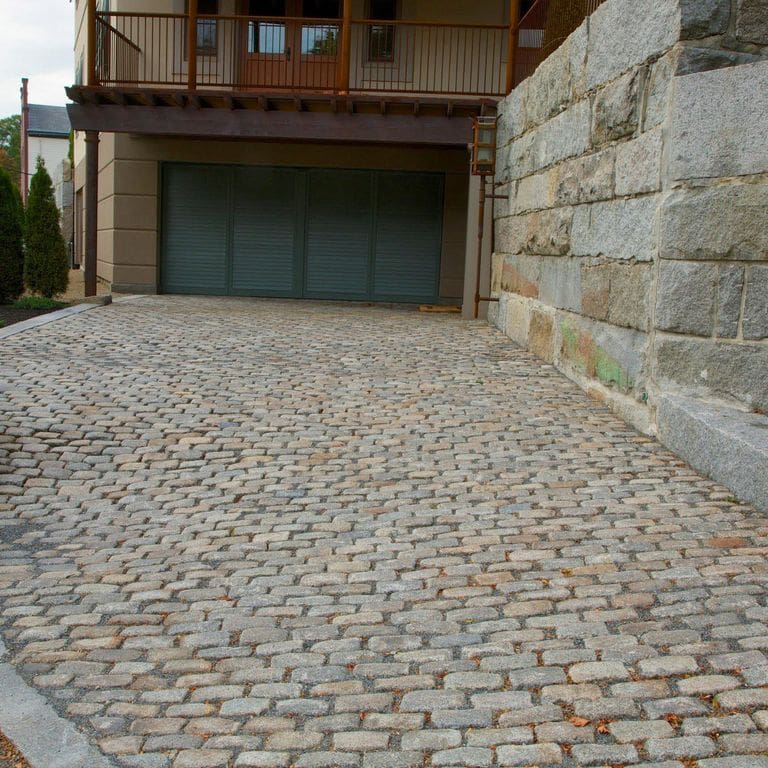The image shows this material being used in a driveway pavers application. The dominant color shown is gray; with brown, orange/rust, white and tan secondaries. The color mix creates a warm feeling. Regular color pattern.