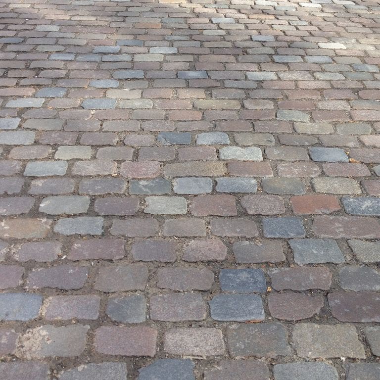 Application image for Granite - Reclaimed Swedish Cobblestones. The image shows this material being used for driveway pavers and path pavers. The surface finish shown is antiqued. The dominant color shown is gray. The color mix creates a warm feeling.