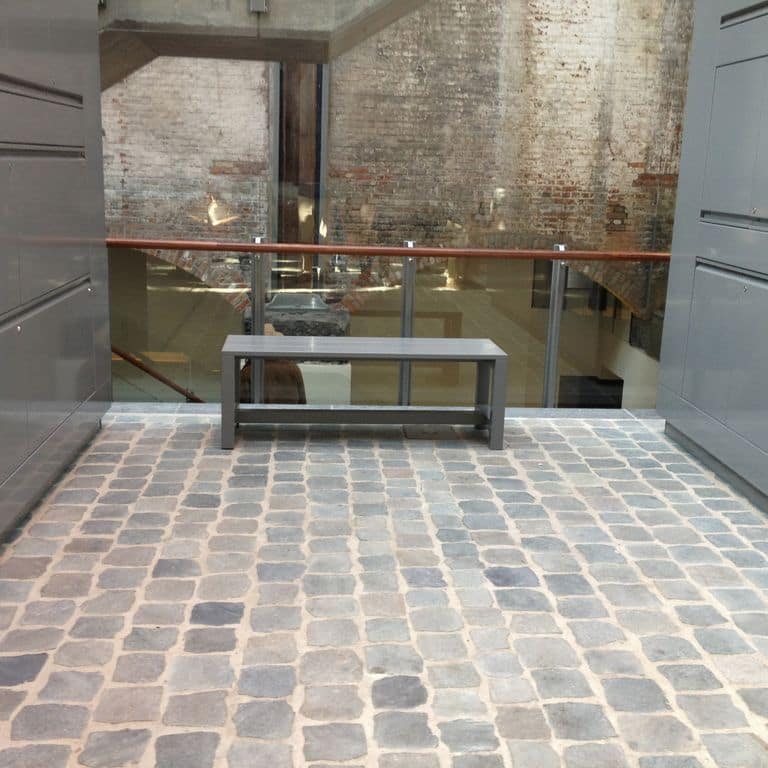 Application image for Porphyry - Reclaimed European Cobblestones. The image shows this material being used in an interior floor application. The surface finish shown is sawn. The dominant color shown is gray. The color mix creates a warm feeling.