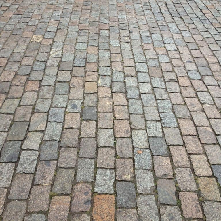 Application image for Reclaimed European Porphyry Cobblestones. The image shows this material being used in a driveway pavers application. The surface finish shown is . The dominant color shown is gray. The color mix creates a warm feeling.