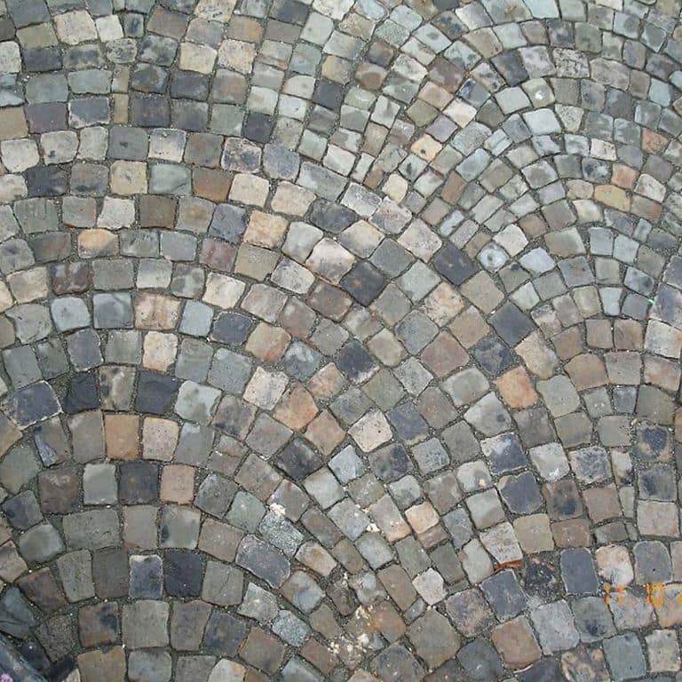 Application image for Reclaimed European Sandstone Cobblestones. The image shows this material being used in a driveway pavers application. The surface finish shown is . The dominant color shown is gray; with beige, black, blue, brown, orange/rust, purple, white and tan secondaries. The color mix creates a cool feeling. Regular color pattern.
