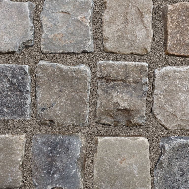 Application image for Reclaimed European Sandstone Cobblestones. The image shows this material being used for driveway pavers, path pavers and patio pavers. The surface finish shown is . The dominant color shown is gray; with beige, black, brown, green, orange/rust, purple, white and tan secondaries. The color mix creates a warm feeling. Regular color pattern.
