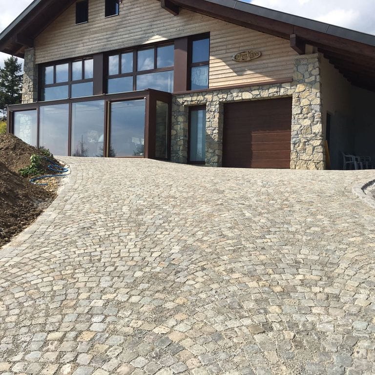 Application image for Reclaimed European Sandstone Cobblestones. The image shows this material being used in a driveway pavers application. The surface finish shown is . Dominant colors shown are beige, gray and tan. The color mix creates a warm feeling.