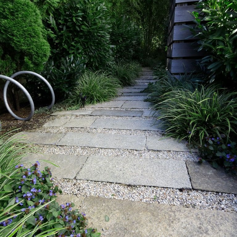 The image shows this material being used in a path pavers application. The dominant color shown is gray; with beige, blue, purple, white, tan and cream secondaries. The color mix creates a cool feeling. Regular and fine speckled color patterns.