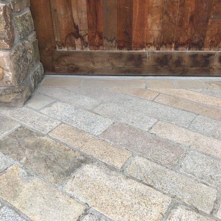 Application image for Reclaimed Footworn Granite Planks. The image shows this material being used for driveway pavers, patio pavers and driveway aprons. The dominant color shown is gray. The color mix creates a warm feeling.