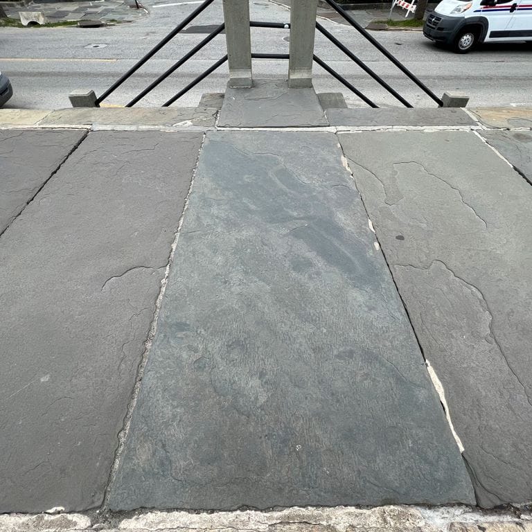 Application image for Reclaimed Bluestone Sidewalk Stones. The image shows this material being used in a path pavers application. The surface finish shown is a combination of natural cleft, weathered and worn. The dominant color shown is gray; with blue and green secondaries. The color mix creates a cool feeling. Regular color pattern.