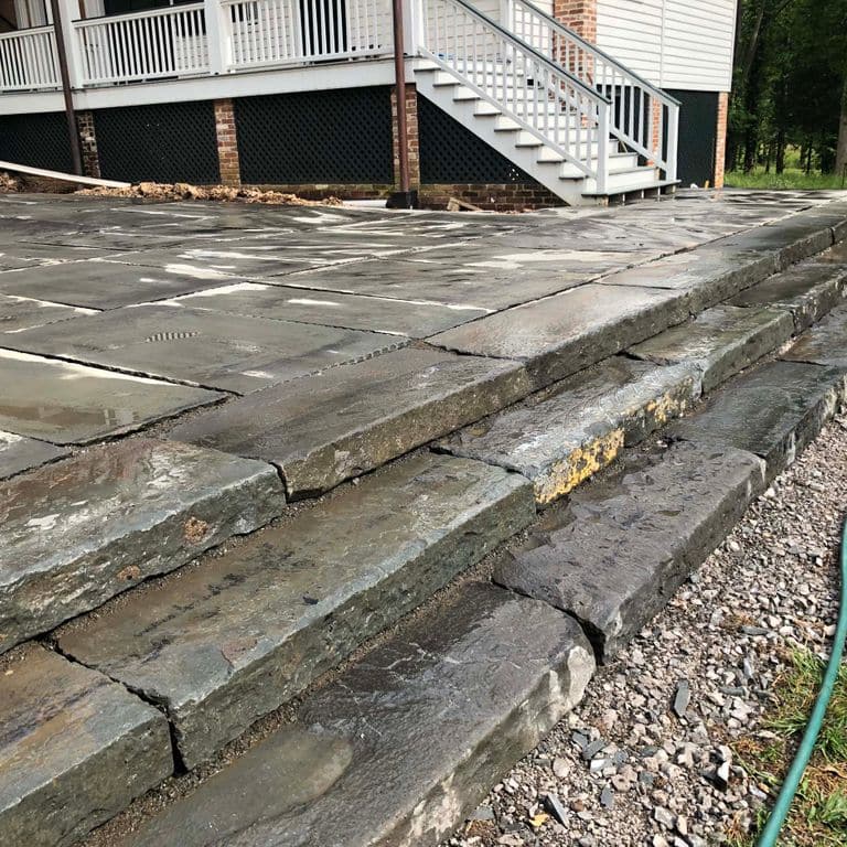 The image shows this material being used for patio pavers and monolithic steps. The dominant color shown is gray; with purple, white, tan and cream secondaries. Regular color pattern.