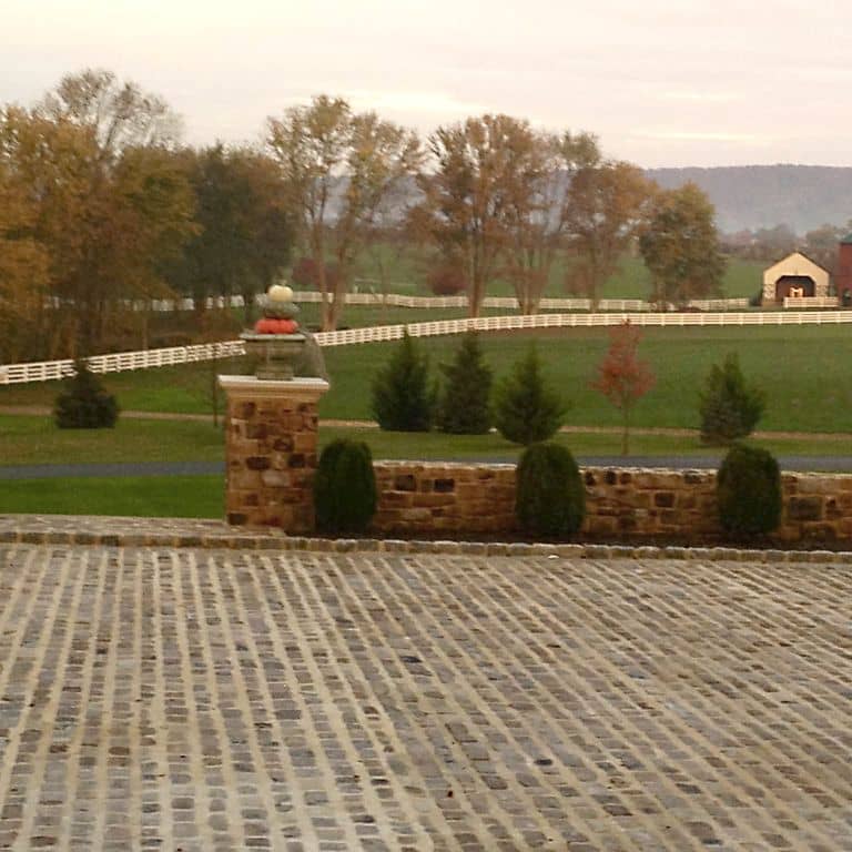 Feature image for Reclaimed Midwest Sandstone Cobblestones. The image shows this material being used for driveway pavers and patio pavers. The dominant color shown is brown; with beige, gray, orange/rust, white, tan and cream secondaries. The color mix creates a warm feeling. Regular color pattern.