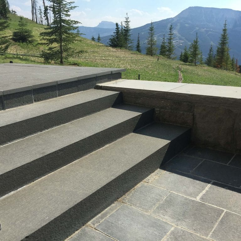 Feature image for Nordic Black Basalt. The image shows this material being used for patio pavers and monolithic steps. The surface finish shown is flamed. Dominant colors shown are black and gray. Regular color pattern.