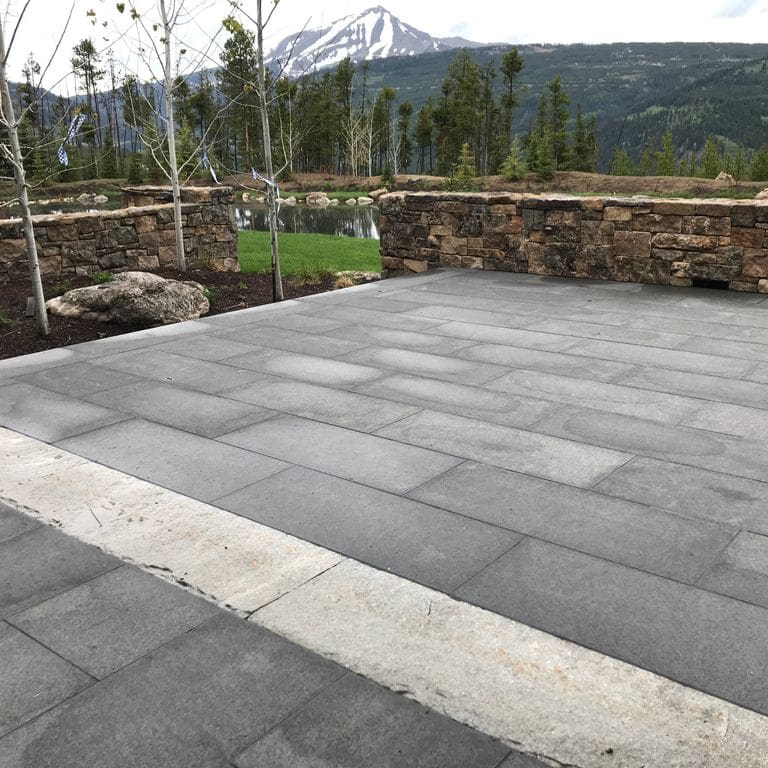 Application image for Nordic Black Basalt. The image shows this material being used in a patio pavers application. The surface finish shown is flamed. The dominant color shown is gray. The color mix creates a warm feeling. Regular color pattern.
