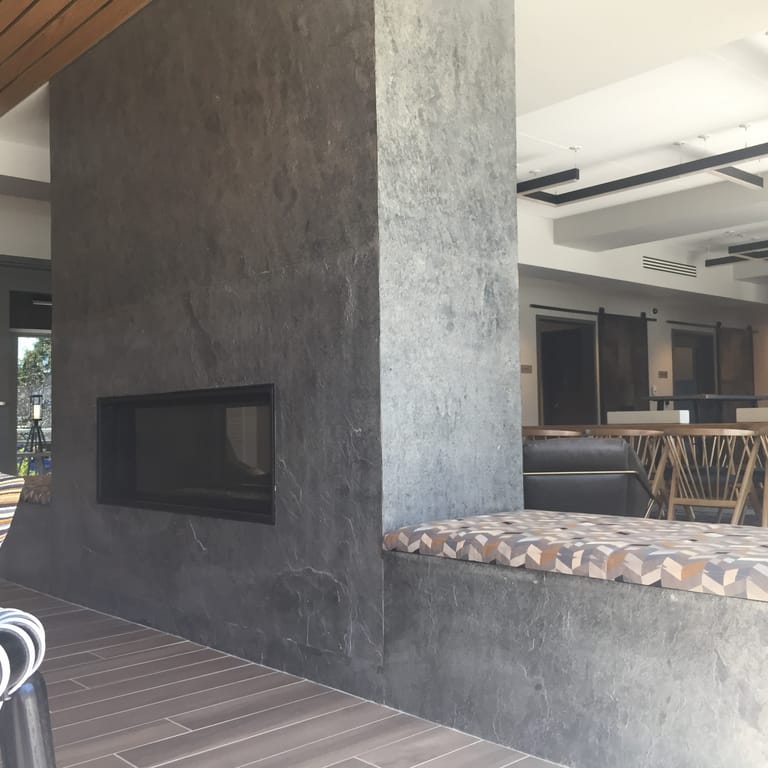 Feature image for Quartzite - Amazon. The image shows this material being used in a fireplace surround application. The dominant color shown is gray; with beige and white secondaries. Exhibits "movement". Regular, blotched and cloudy color patterns. Contains some mica and mineral inclusions.