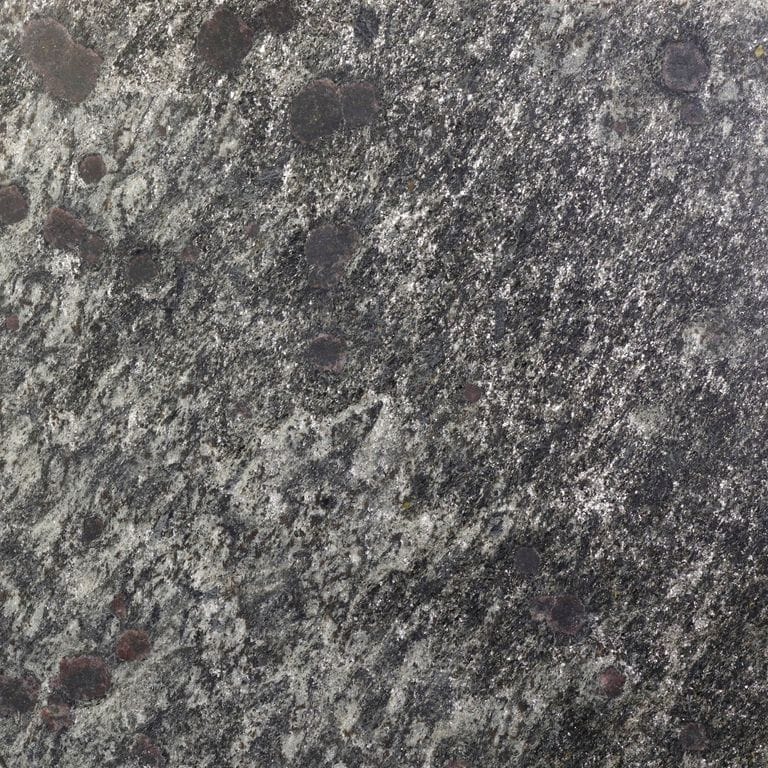 Close-up image for Metal Dust Quartzite. The surface finish shown is honed. The dominant color shown is gray; with black, brown, green, purple and white secondaries. Exhibits "movement" and the color mix creates a cool feeling. Speckled, coarse speckled, blotched and linear color patterns.