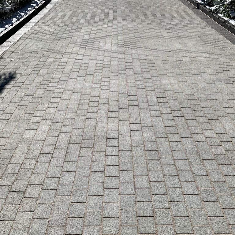 Feature image for Italian Bluestone. The image shows this material being used in a driveway pavers application. The dominant color shown is gray; with green and purple secondaries. The color mix creates a cool feeling. Regular and fine speckled color patterns.
