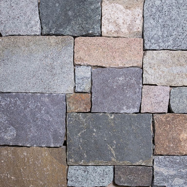 Best close-up image for Adirondack Granite. The surface finish shown is split-face. The dominant color shown is gray; with beige, blue, brown, green, orange/rust, pink, purple, white and tan secondaries. Regular, fine speckled and cloudy color patterns.