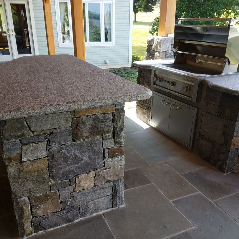 Feature image for Dolph Pond Granite. The image shows this material being used in a thin veneer application. The dominant color shown is gray; with blue, brown, green, orange/rust, purple, white and tan secondaries. The color mix creates a warm feeling.