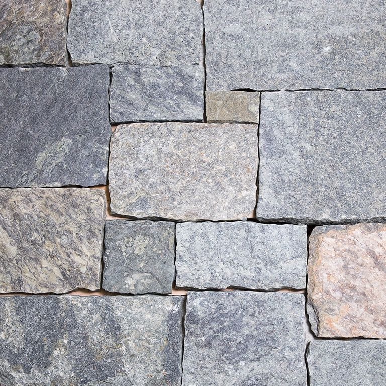 Best close-up image for Blue Mountain Granite. The image shows this material being used for full bed veneer and thin veneer. The surface finish shown is a combination of split-face and weathered. Dominant colors shown are blue and gray; with beige, orange/rust, pink, purple, white and tan secondaries. Exhibits "movement". Regular, fine speckled, blotched and cloudy color patterns.
