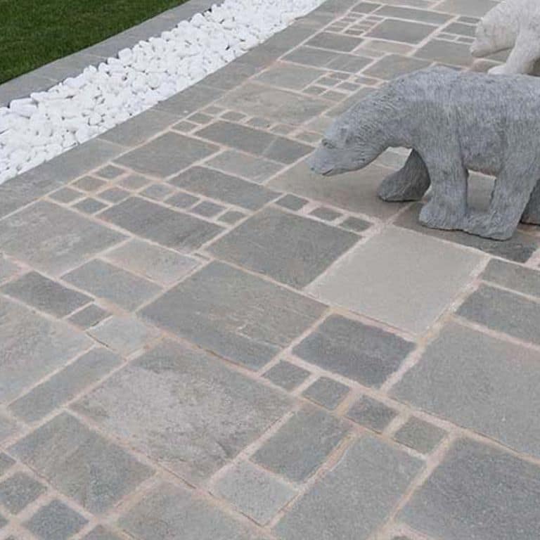 Feature image for Greek Quartzite Slate - Grey. The image shows this material being used in a patio pavers application. The dominant color shown is gray; with beige, blue and white secondaries. Exhibits "movement" and the color mix creates a cool feeling. Regular, fine speckled and cloudy color patterns.