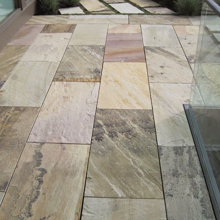 Feature image for Fossil Rustic Sandstone. The image shows this material being used for interior floor and patio pavers. The surface finish shown is natural cleft. Dominant colors shown are beige, brown, green, gray, purple and tan; with black, orange/rust, white and cream secondaries. The color mix creates a warm feeling. Streaked, veined, blotched and random color patterns.