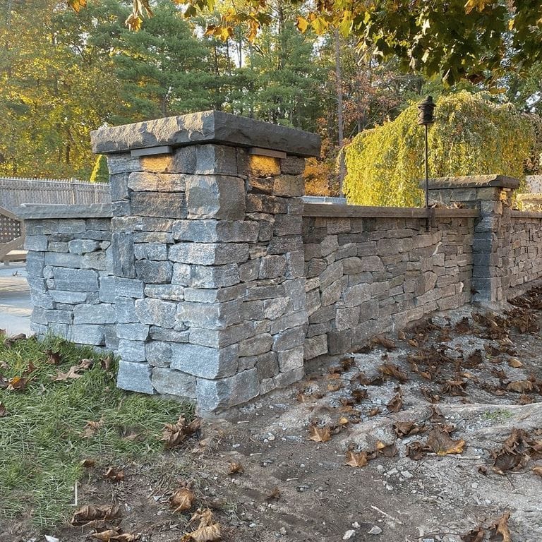 Application image for Black Ash Granite. The image shows this material being used for full bed veneer and thin veneer. The surface finish shown is split-face. Dominant colors shown are green and gray; with beige, blue, orange/rust, purple and tan secondaries. Regular color pattern.